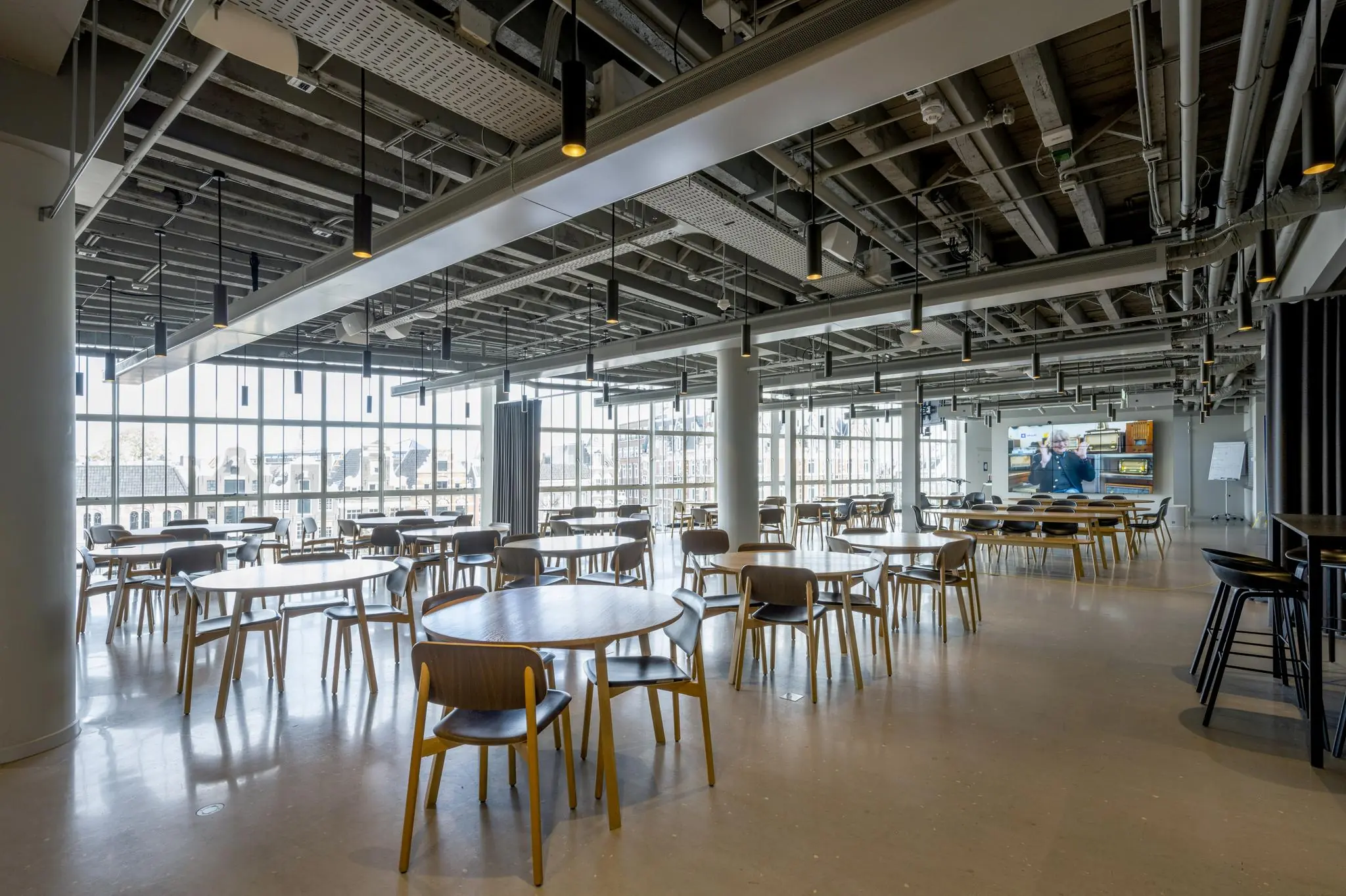 Moderne, open kantineruimte met houten tafels en stoelen in het gebouw aan de Sint-Jorissteeg.